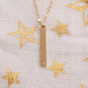 Detail einer goldenen Halskette mit Balkenanhänger und Zirkon-Inlay auf Sternenmuster-Hintergrund