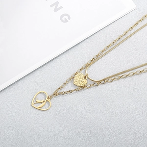 Detail of gold layered heart necklace with textured pendant and couple silhouette charm