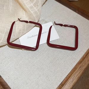 Detail view of deep red geometric hoop earrings with polished lacquer finish on display