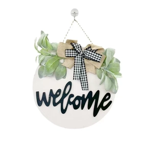 Round wooden welcome sign with green foliage and black and white buffalo plaid bow
