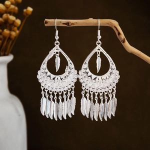 Detailed close-up of Bohemian silver leaf tassel earrings hanging on a natural branch