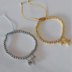 Adjustable gold and silver beaded bracelets with metallic balloon dog charms on gray surface