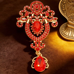Detailed macro view of vintage gold-plated brooch with red crystals and teardrop pendant