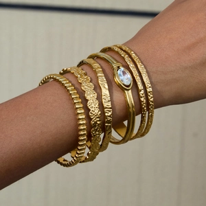 Dettaglio del set di bracciali in acciaio dorato con texture martellata e zircone