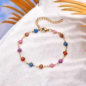 Close-up of golden heart charm bracelet with colorful glitter pendants on white sand