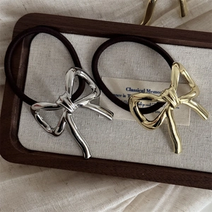 Polished gold and silver metal bow hair ties on elegant dark wood and linen background