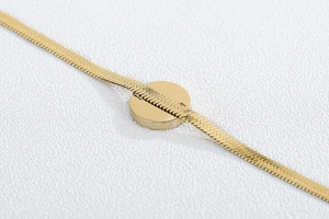 Detail of gold snake bone chain passing through a polished round pendant for women
