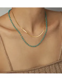 Detail of layered gold snake chain and turquoise beaded necklace on model