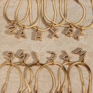 Macro detail of 18K gold plated snake chains with pearl-inlaid initial pendants on marble