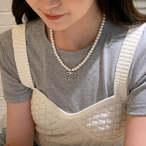 Detailed view of elegant pearl necklace with silver bow pendant on a female neck
