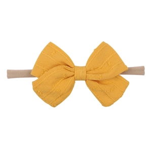 Detailed macro view of mustard yellow Swiss dot fabric bow on a soft nylon baby headband