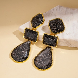 Détail de boucles d'oreilles géométriques en résine avec monture dorée et reflets noirs