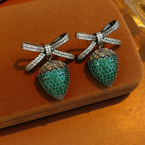 Macro detail of vintage strawberry bow earrings with green crystals on brown velvet