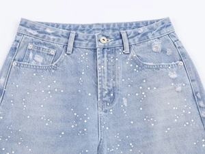 Détail de taille en jean bleu clair avec ornements de perles blanches et tissu usé