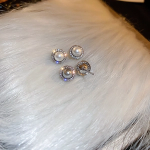 Detailed view of elegant pearl stud earrings with zircon halo on white faux fur background