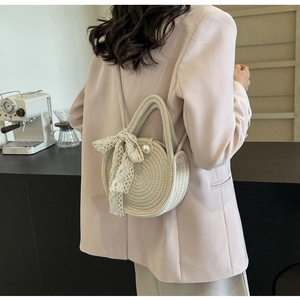 Detail of hand-woven off-white round bag with lace bow and pearl accents on model