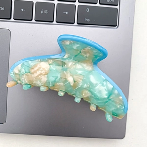 Detail of blue and beige marbled acetate hair claw clip on a silver laptop keyboard