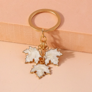Detail of a gold keychain featuring three white ginkgo leaf pendants on a warm background