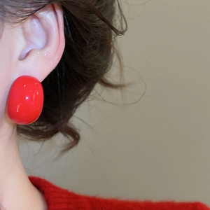 Close-up of gloss red acrylic drop earring worn on ear with vibrant red sweater