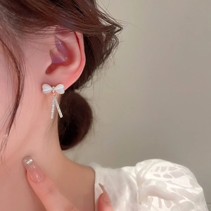 Détail de boucles d'oreilles nœud avec pierres œil de chat et pompons en strass