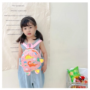 Toddler girl wearing pink cartoon dinosaur backpack against a minimalist soft wall background