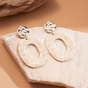 Macro detail of textured silver metal and wavy cream oval earrings on a stone base