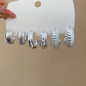 Detail showing three pairs of silver C-shape hoop earrings with various textures