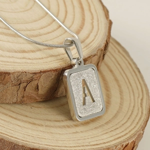 Silver stainless steel snake chain with a hollow letter A pendant on a wood piece