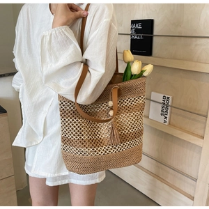 Detailed view of woven straw tote bag with brown PU leather strap and tassel charm