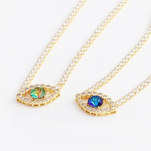 Gold evil eye necklace with green and blue zircon crystals in a high-quality flat lay view
