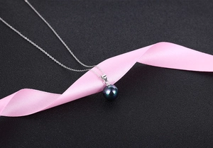 Detailed close-up of dark iridescent pearl pendant on a fine silver chain with pink silk ribbon