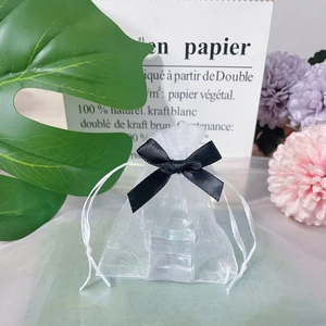 Detailed view of small white organza gift bag with black ribbon and floral background