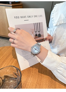 Close-up of elegant silver quartz watch with diamond bezel worn on a wrist in a cafe setting