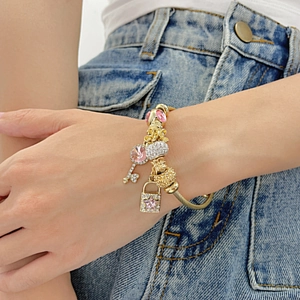 Golden beaded cable bracelet with pink crystal key and lock charms on woman's wrist