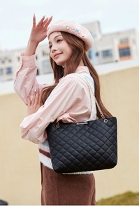 Détail d'un sac cabas noir matelassé avec logo doré et bandoulière chaîne sur un mannequin