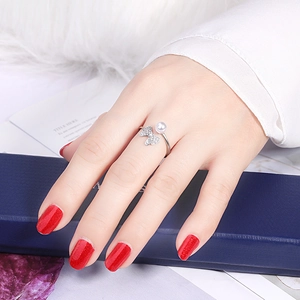 Detailed close-up of an open silver ring with a white pearl and zircon bow on a finger