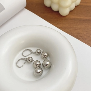 Close-up of silver drop earrings featuring three graduated metal beads on a white tray