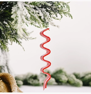 Detail of red and white spiral acrylic candy cane hanging on snow-covered pine branch