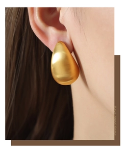 Close-up of a matte gold teardrop earring with brushed metal texture on a female model