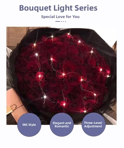 Detail view of red rose bouquet wrapped in black mesh with warm LED string lights