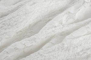 Close-up of white lace fabric featuring floral hollow-out and textured bubble patterns