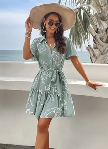 Detailed view of a green floral short sleeve dress with belt and ruffled hem by the beach
