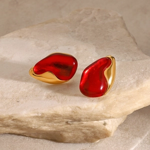 Close-up of irregular gold-plated stud earrings with deep red resin on a natural stone