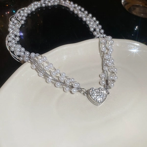 Detail of multi-layer pearl necklace with a sparkling diamond-set heart pendant on ceramic