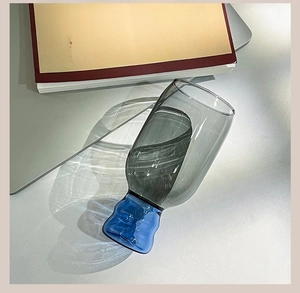 Artistic high-angle view of a grey glass cup with a blue wavy base on a sunlit desk