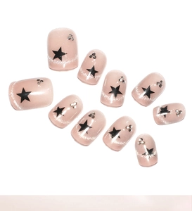 Macro detail of nude pink press-on nails with black stars and silver glitter french tips