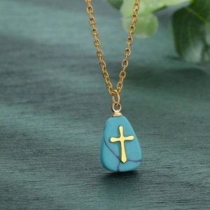 Detailed close-up of a gold cross on a turquoise stone pendant necklace over dark wood