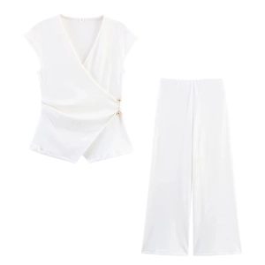 Detalle de top blanco cruzado con hebilla dorada y pantalones de pernera ancha