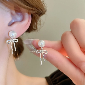 Élégantes boucles d'oreilles nœud argentées avec perles blanches sur un mannequin