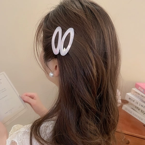 Detail view of pearlescent oval hair clips and pearl studs worn by a model in a cozy setting